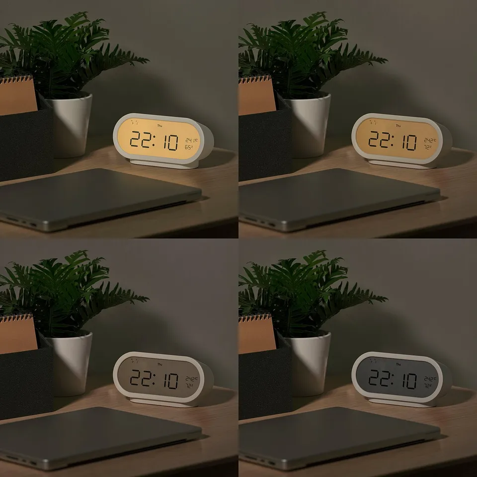 Four illuminated clocks displaying 22:10, with plant, laptop, and notebook on a desk, varying screen brightness.