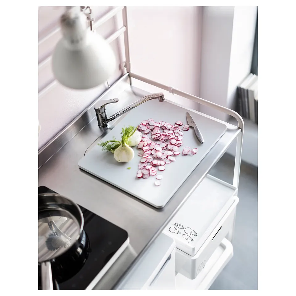 SUNNERSTA mini-kitchen in white, stainless steel sink, cutting board with sliced radishes and knife.