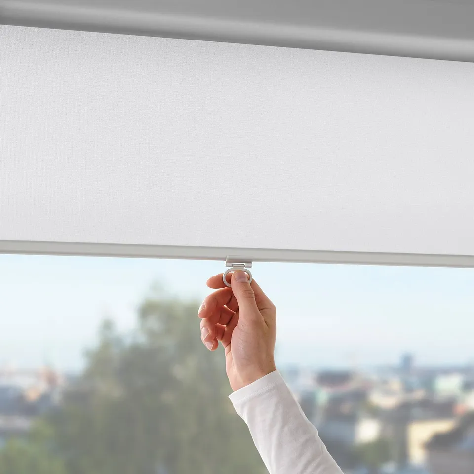Hand pulling cordless white roller blind, blocking light, mounted on window.