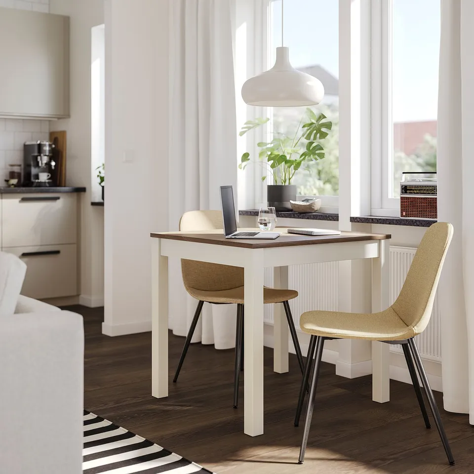 Small, cosy dining setup. White NORDMANSSKÄR chair with tan seat. Modern design with wooden table and pendant light.