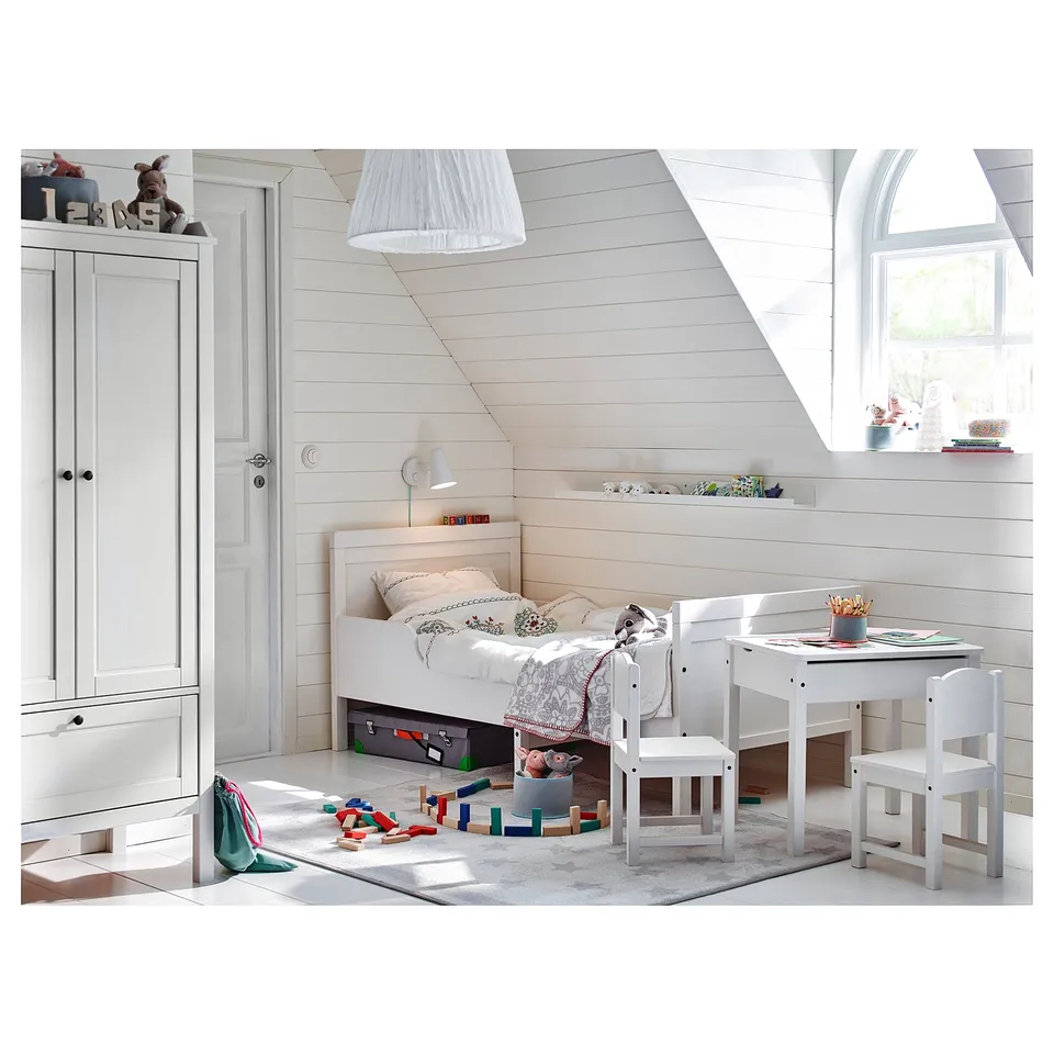 Childrens bedroom with white furniture: bed, desk, chair, and wardrobe. Toys and books are scattered around.