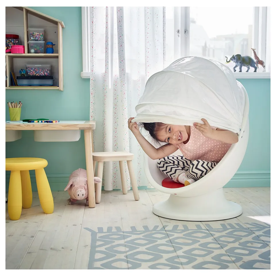 Girl in white IKEA chair, room with yellow stool, table & toy.