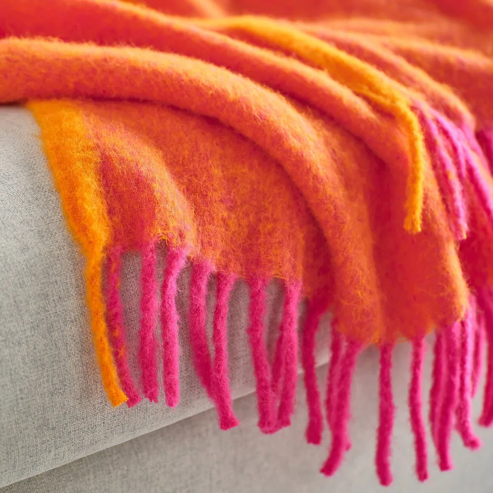 Vibrant throw blanket, incredibly soft & fluffy, made from recycled polyester, displayed on grey fabric.