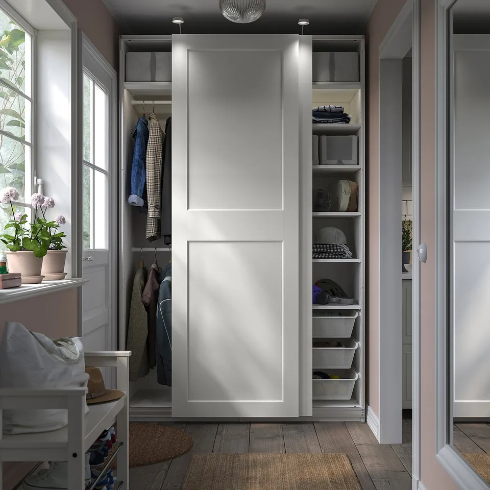 Modern wardrobe with sliding doors, organised storage, adjustable shelves, and hanging space. Light grey, wooden floor, and potted plants nearby.
