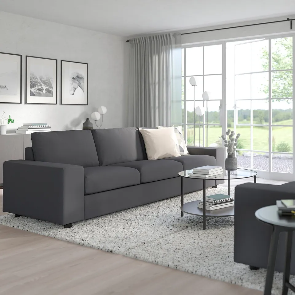 Modern living room with grey VIMLE sofa, white pillows, large windows, rug, coffee table, and wall art. Sofa suited for relaxation and conversions.