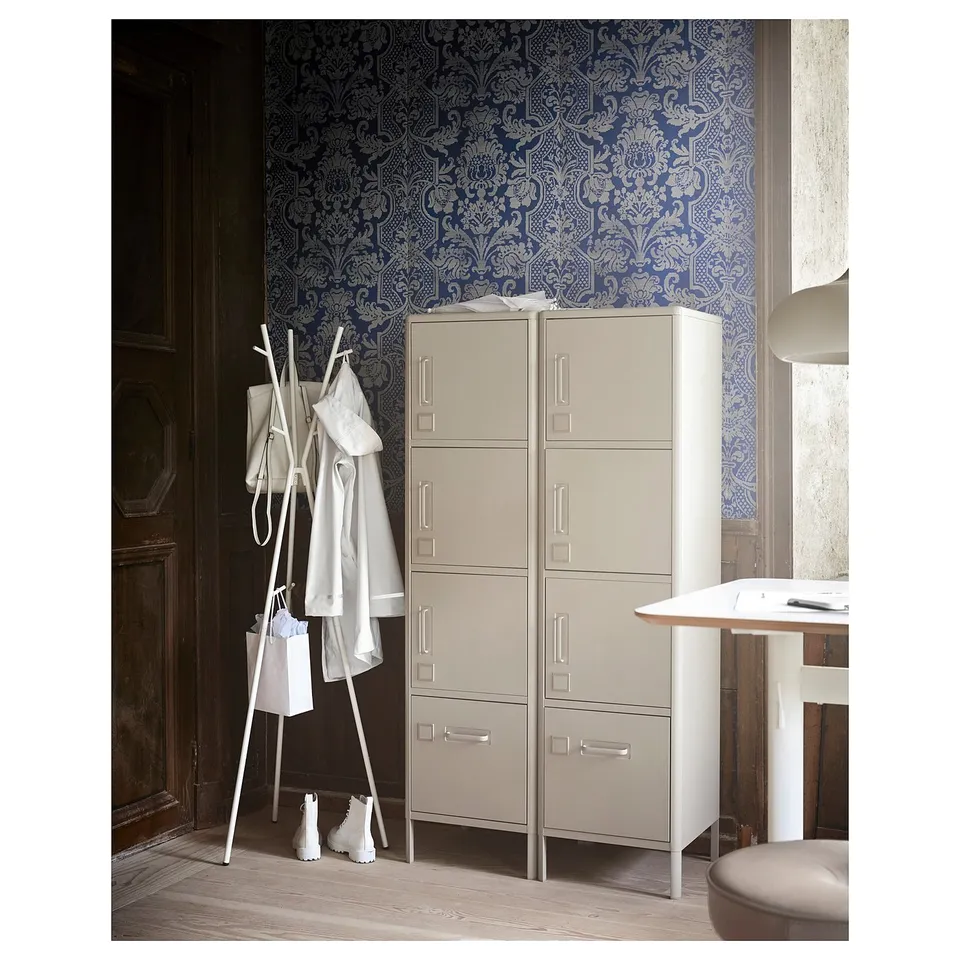 IDÅSEN storage unit: cream-colored metal cabinet with multiple drawers and doors, against blue patterned wallpaper.