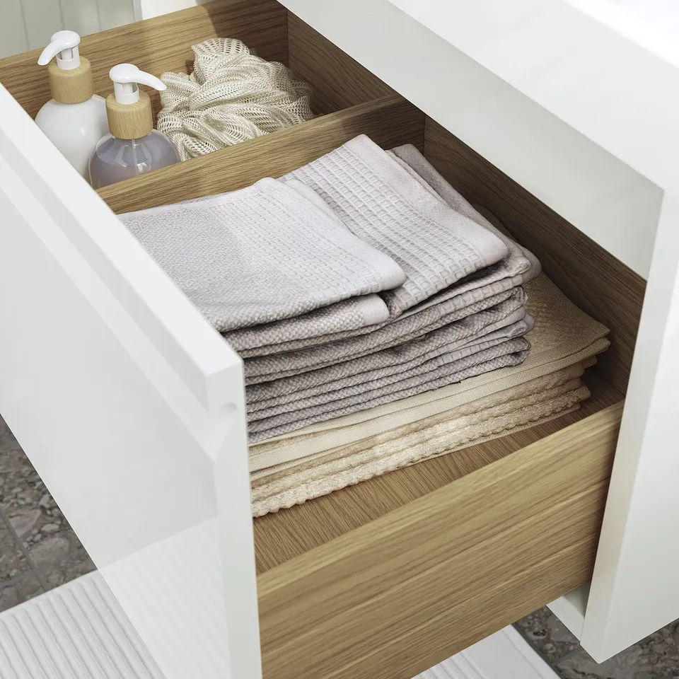 Open bathroom drawer with neatly folded towels and bottles, showing organised storage.