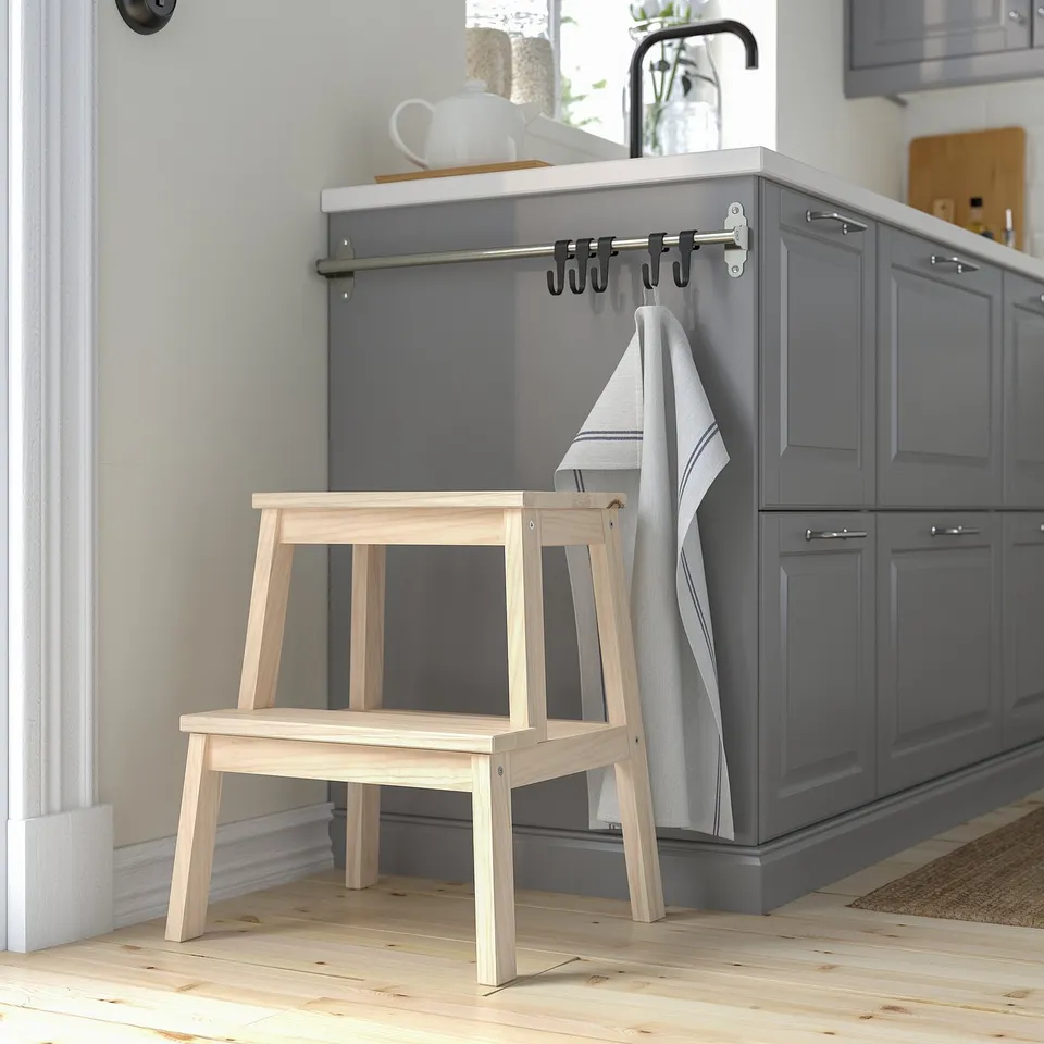 Minimalist wooden step stool in natural wood beside grey kitchen cabinets, blending size with surroundings.