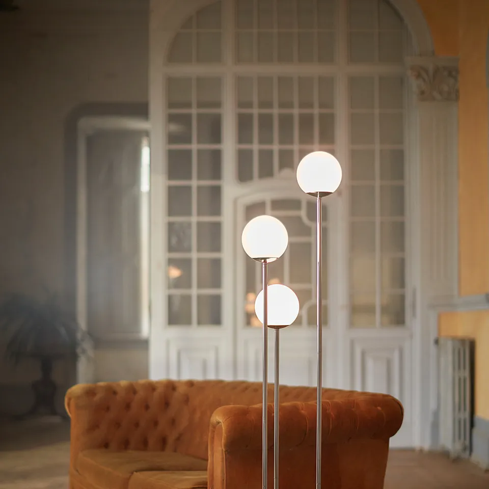 Modern living room with orange sofa, rug, and chrome lamp by large window.