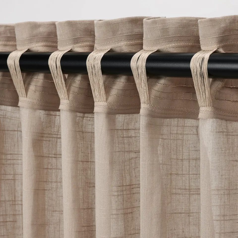Beige SILVERLÖNN curtains with linen texture hang neatly from rods, allowing light while softening glare, with a heading tape for easy pleating.