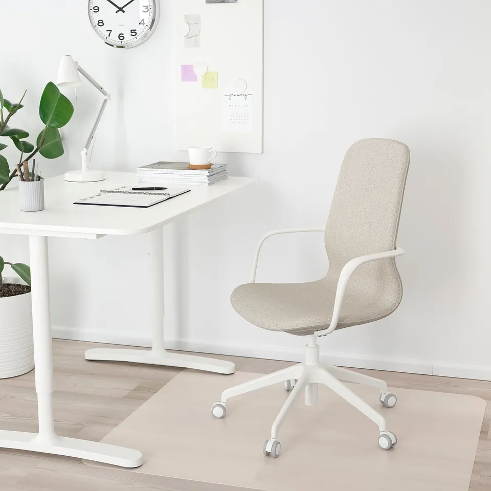 A minimalist white home office with a LÅNGFJÄLL chair in beige, a white table, and a wall clock. The chair fits perfectly under the table.