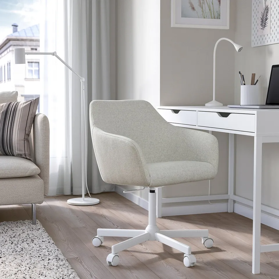 Modern home office: white TOSSBERG chair fits under white desk by window, near grey sofa.