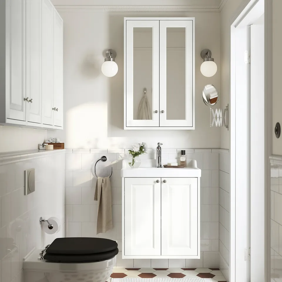 White TÄNNFORSEN bathroom with bevelled vanity, tall mirror, black toilet, patterned floor, and round lights.