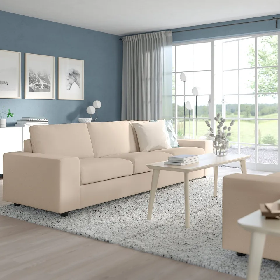 Modern living room with light beige VIMLE sofa, coffee table, and large window offering outdoor view. Blue painted walls and grey curtains.