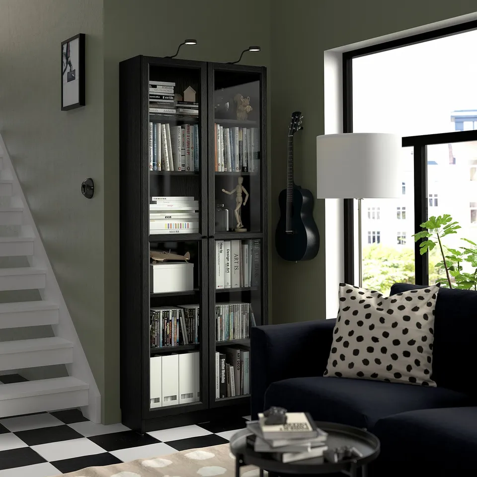 Dark wood BILLY bookcase with guitar, sofa & staircase in monochrome room.