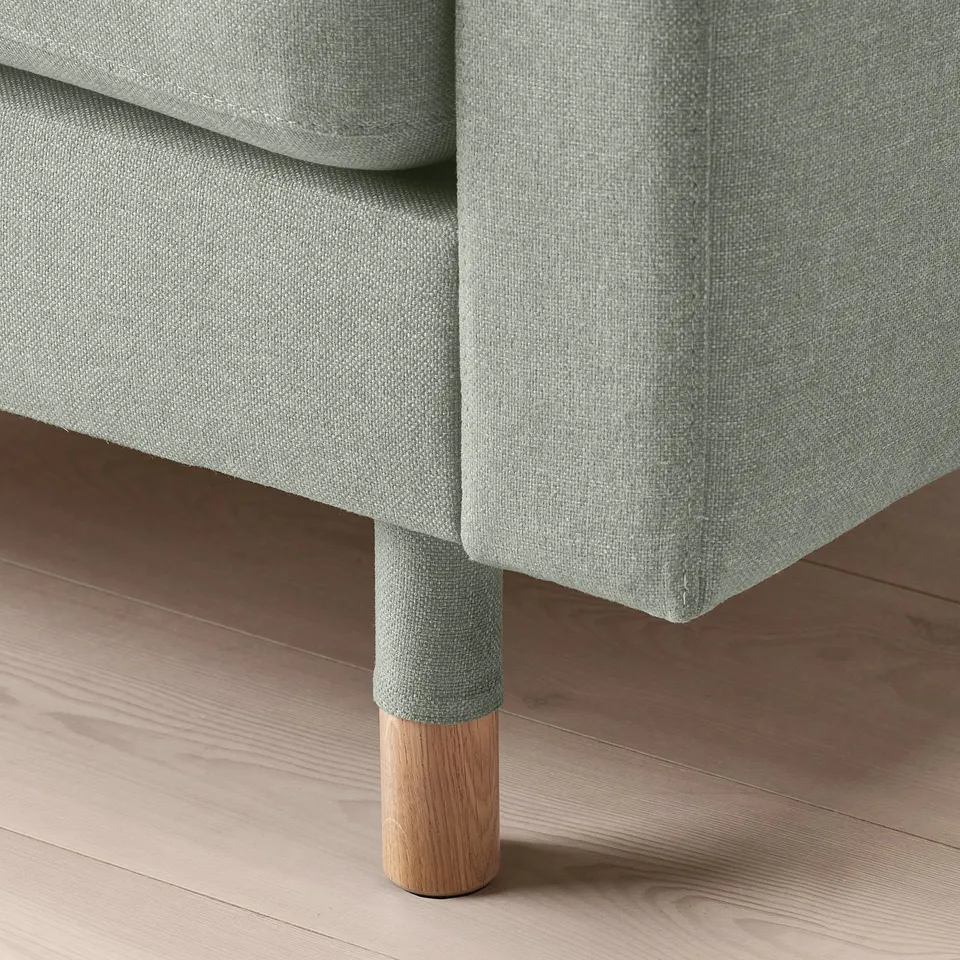 Light green sofa with wooden legs on wooden floor. High resilience cushions, neat design.