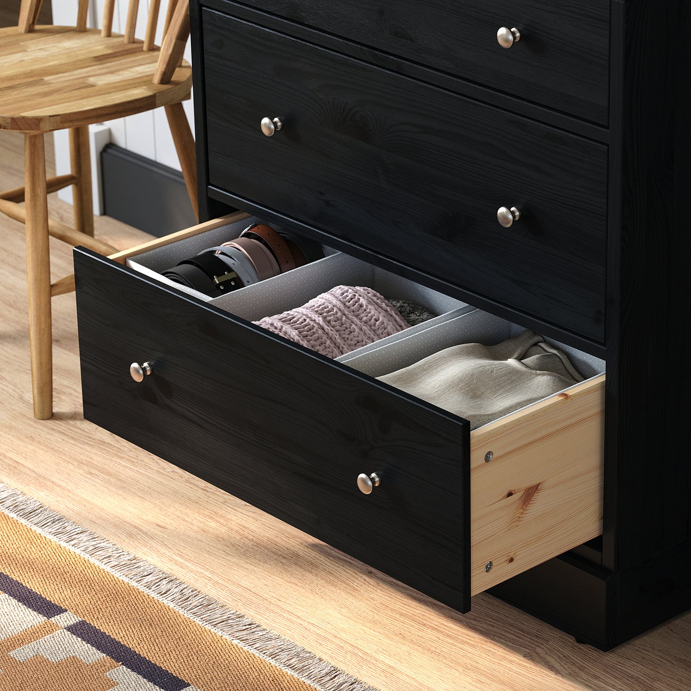 Black wooden chest of drawers with an open drawer revealing compartments and folded clothes. The drawer pulls out smoothly.
