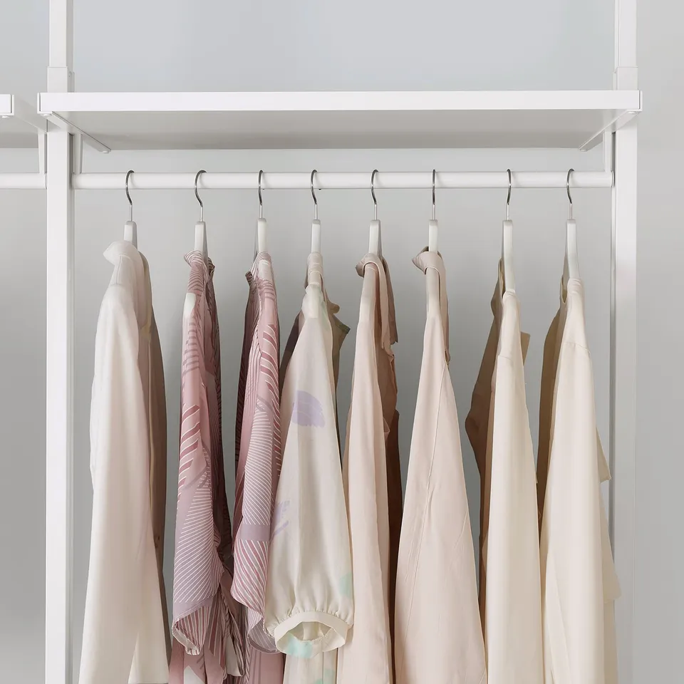 A white closet with adjustable shelves and hanging rail displays neatly arranged clothes on hangers, showcasing its customizable storage solution.