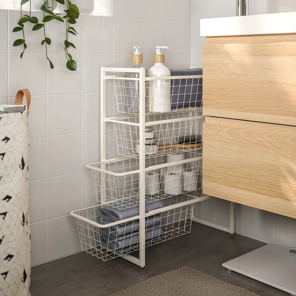 White JONAXEL wire storage rack with bathroom essentials next to wooden vanity.