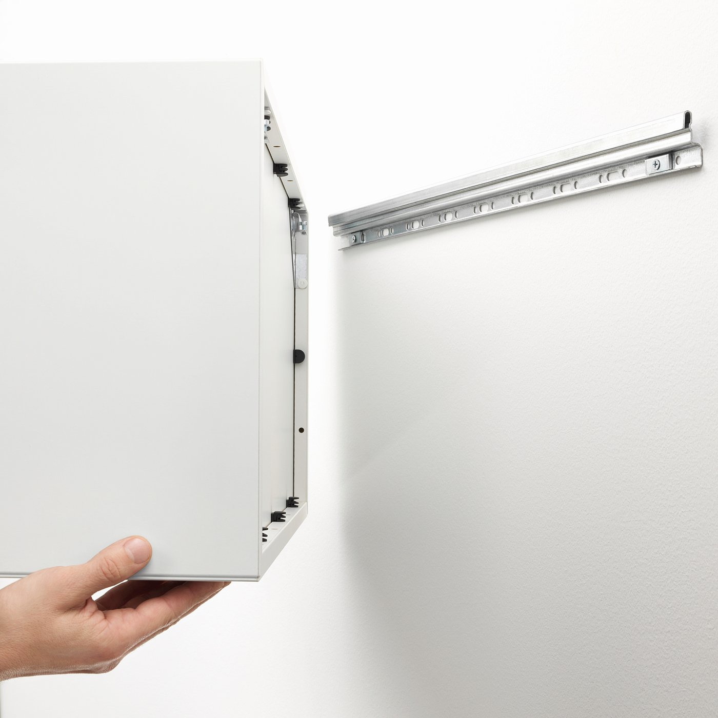 A hand holding an open, wall-mounted EKET cabinet, showing its storage space and suspension rail.