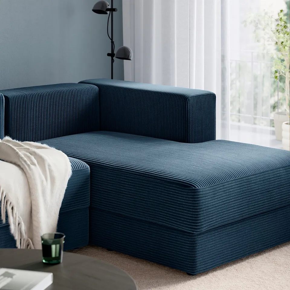 Couch with ottoman, soft pillows, blanket, lamp, glass, book, and window.