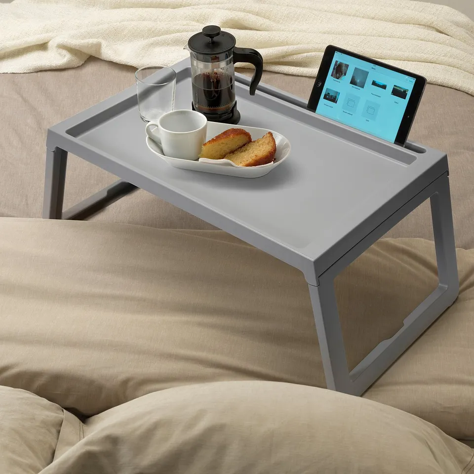 Grey bed tray on bed holds coffee, food, and tablet, with visible cable hole.