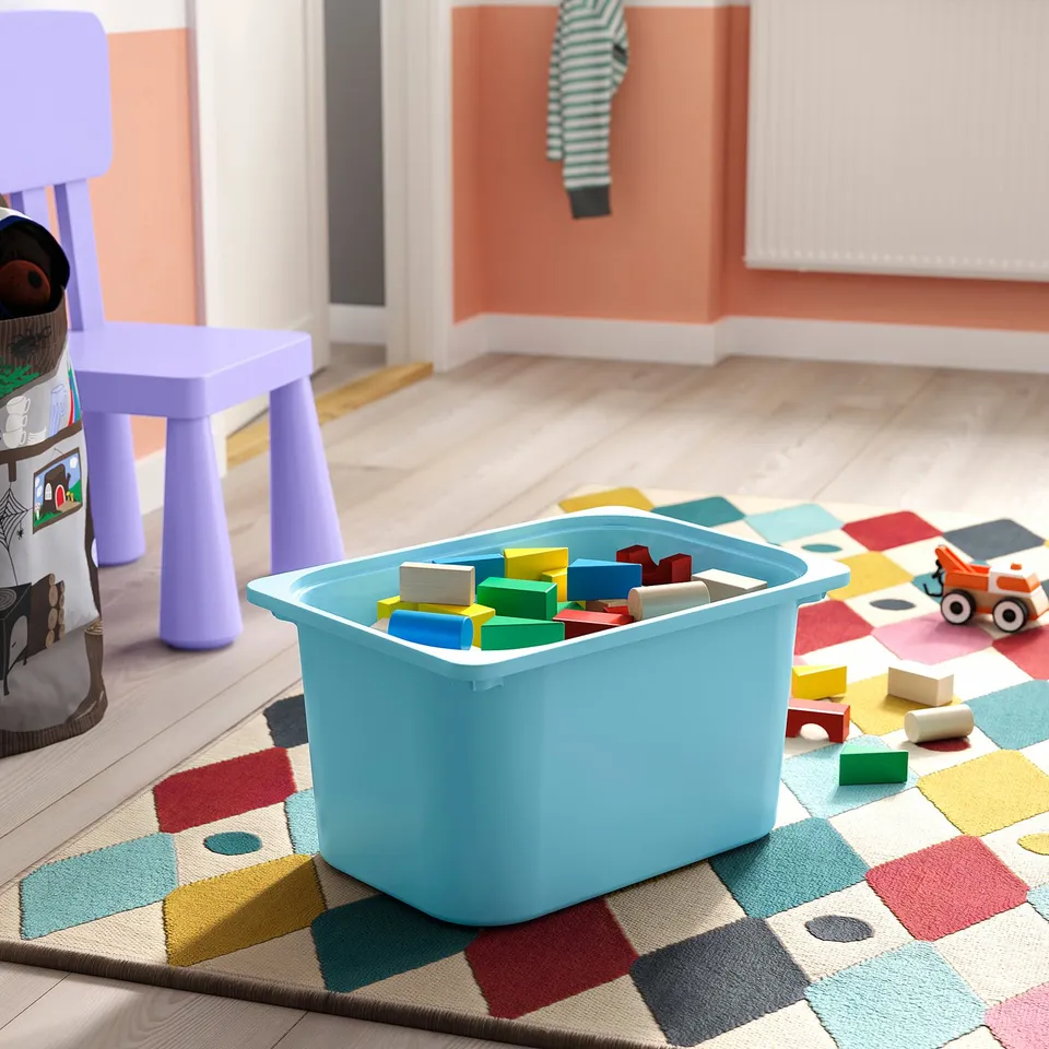 Colourful TROFAST toy storage on rug with truck and chair.