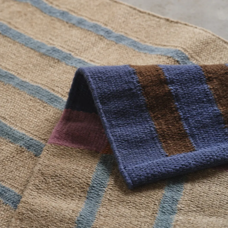 Striped woven rug showing intricate texture, blending hues like beige, blue, and brown. Natural and wool fibres evident.
