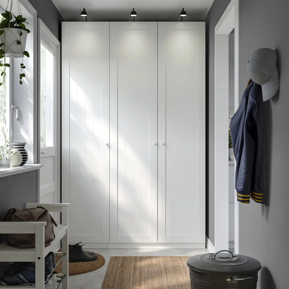 White PAX wardrobe with closed doors. Includes a bench, coat hooks with jacket and hat, and rug. Modern, minimalist design. Large, fits corner space.