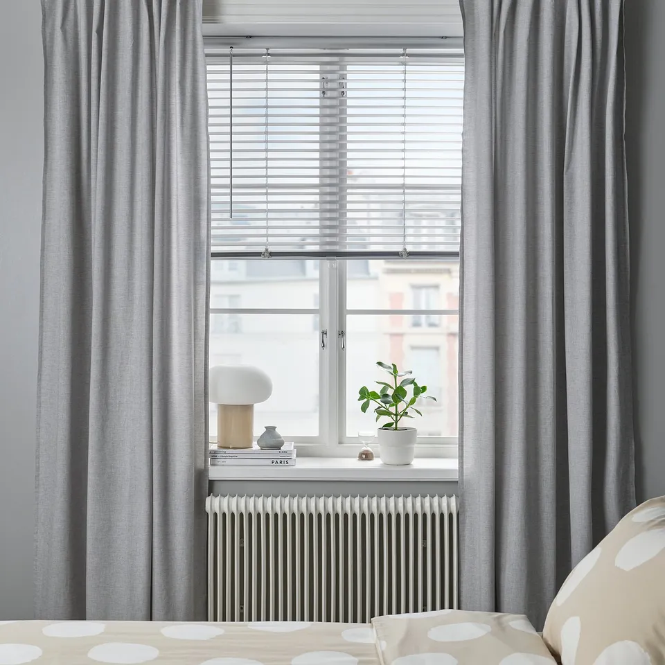 Modern bedroom window with silver VECKLARFLY blinds, curtains, plant, bed.