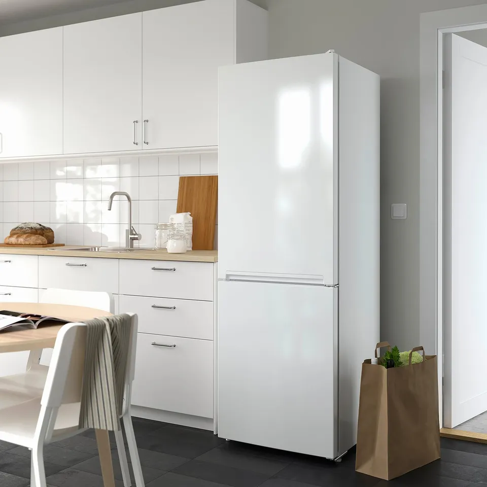 A modern kitchen with a large, tall white VINDÅS fridge/freezer. It has integrated handles and stands prominently next to a window.