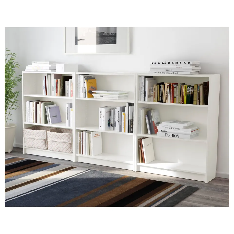 White bookshelves filled with books and decorative bins on colourful rug. BILLY bookcase.