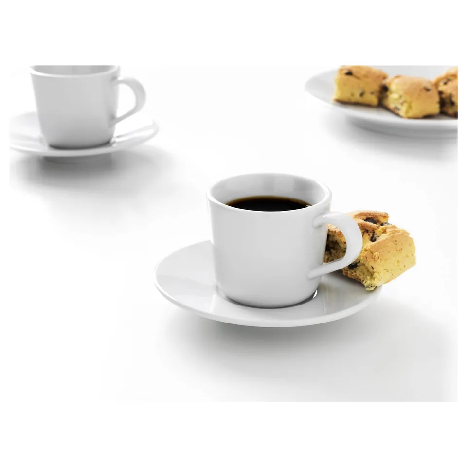 Two white coffee cups on saucers, one with a biscotti cookie, on a white surface.