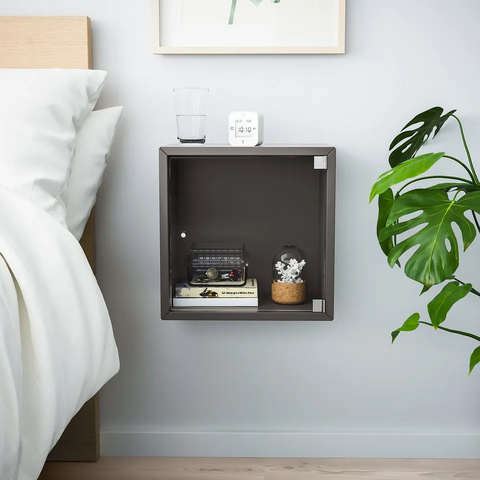 Modern bedroom with white bed, black EKET storage cube, radio, books, plant.