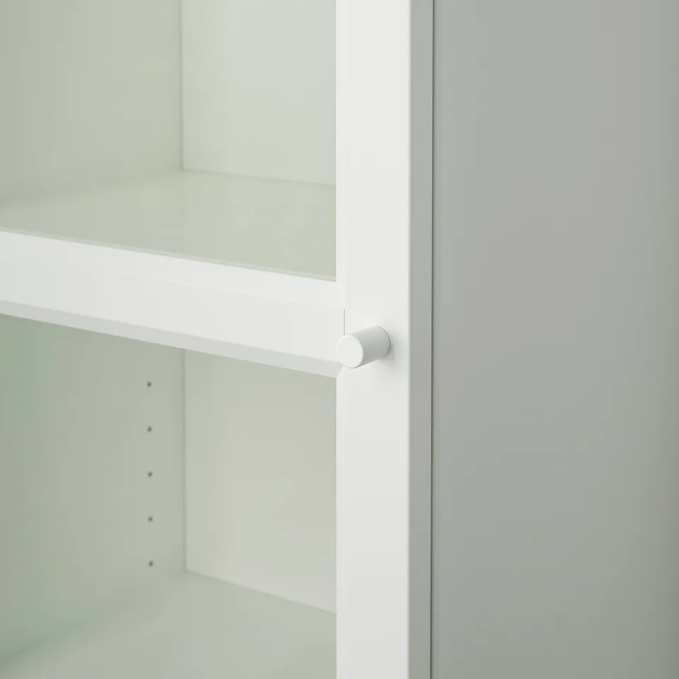 White cabinet with glass door showing adjustable hinge, set against a light wall.