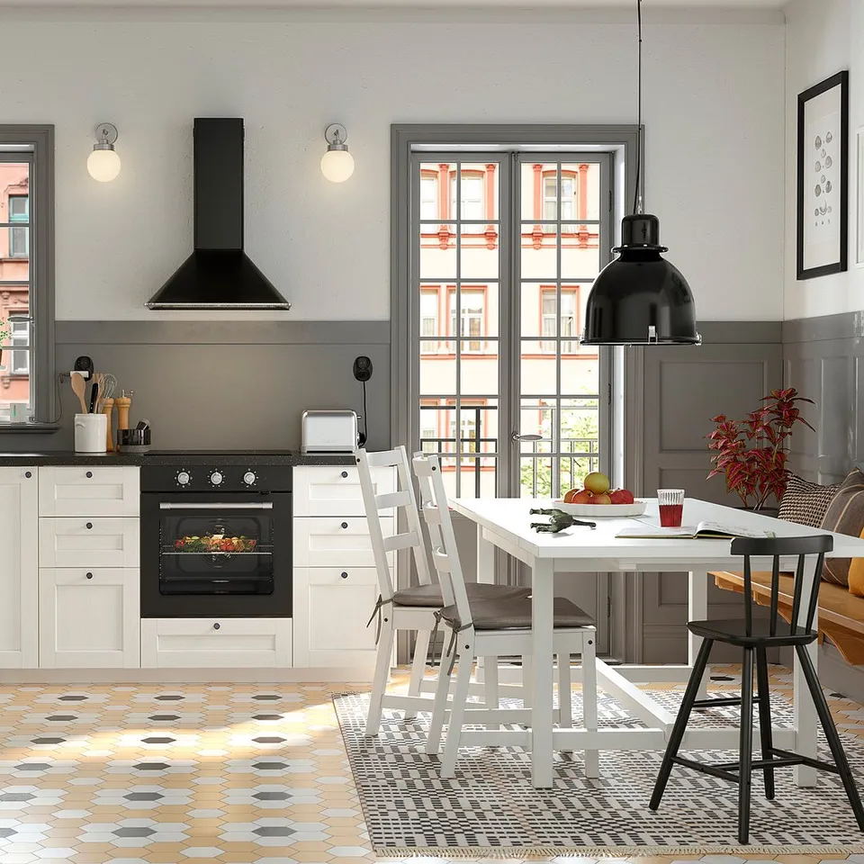 Modern kitchen with white cabinets, black appliances, hexagonal tiles, and a dining area under a black pendant light.