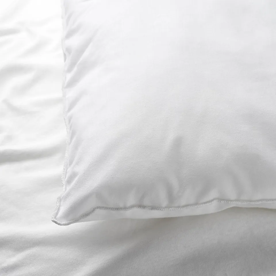 Close-up of soft, white cotton pillowcase, neatly stitched, resting on a bed.