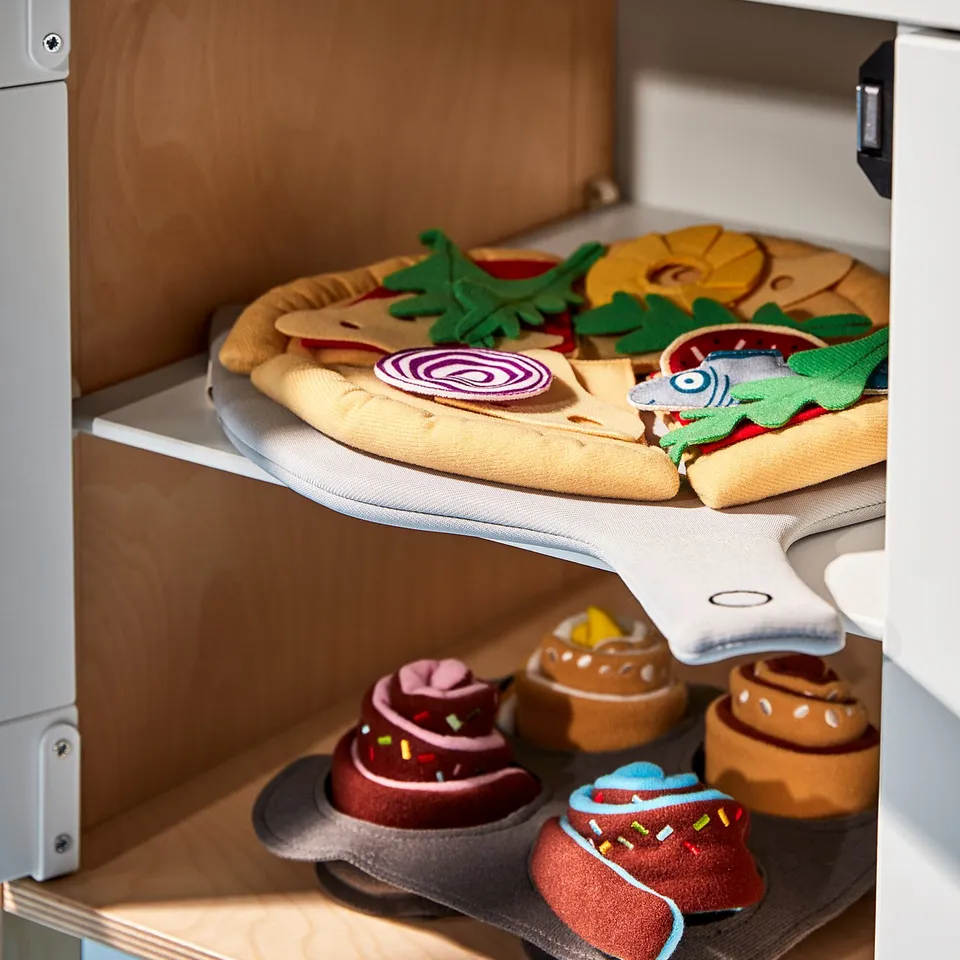 A wooden play kitchen set with fake pizza and baked goods in bright colours.