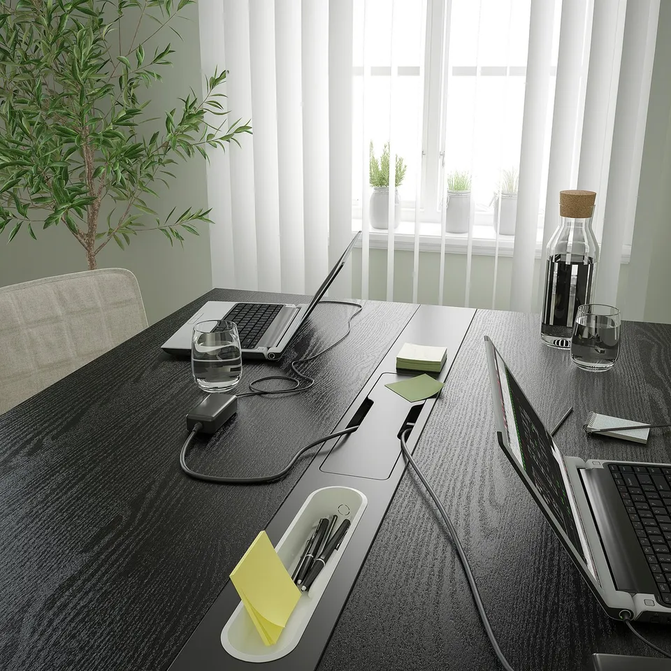 Modern dark office table with charging stations, water, and laptops.