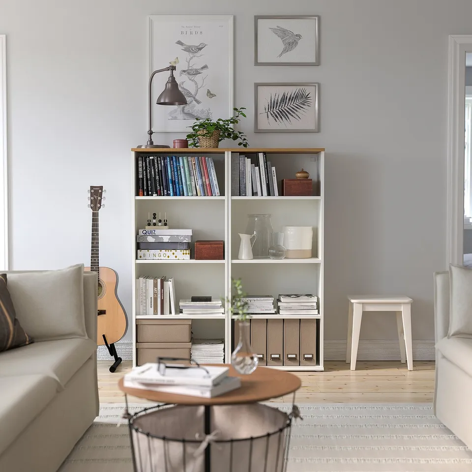 Living room with SKRUVBY bookcase, decorated with plants and art. Armchair left, stool right.