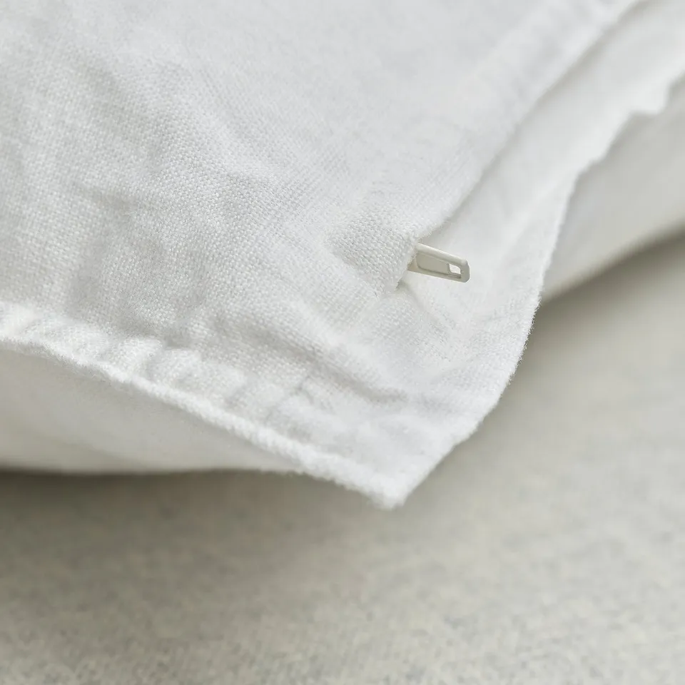 Close-up of soft, white linen cushion cover with subtle texture and discreet zip.