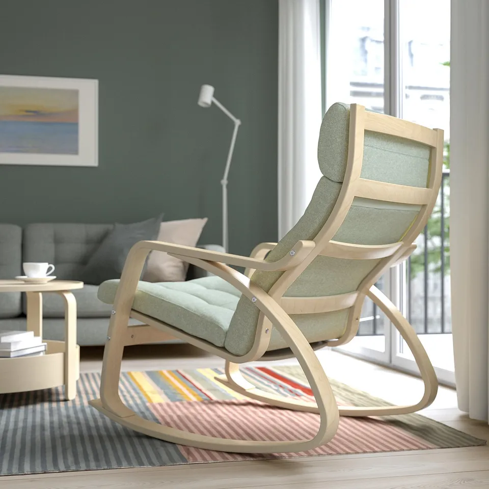 A light wood rocking chair with grey cushions is positioned near a window, providing a relaxing spot to unwind with a calm atmosphere.