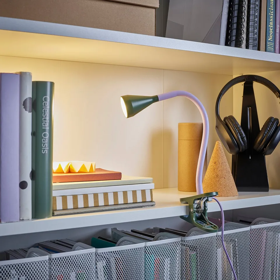 A bookshelf with a lamp clamped on, illuminating books and headphones.