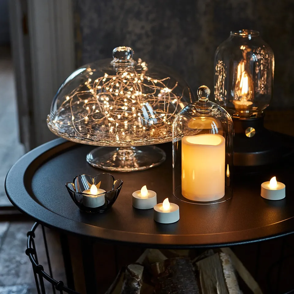 Clear glass dome with led lights on black metal table. Three lit tea lights, one large candle. Cosy, soft lighting ambiance.