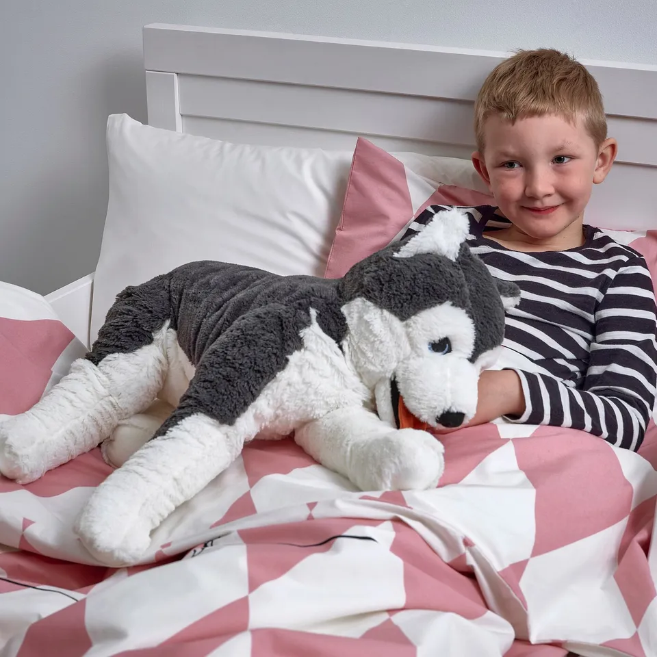 Boy hugs husky toy on patterned bed.