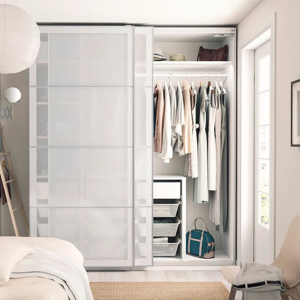 Modern bedroom with open white PAX wardrobe showing clothes, bags, and organisers.