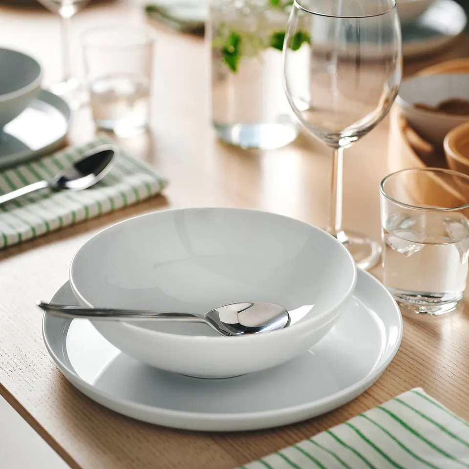 Table set with white bowl and spoon, wine glass, water glass, and green striped napkin.