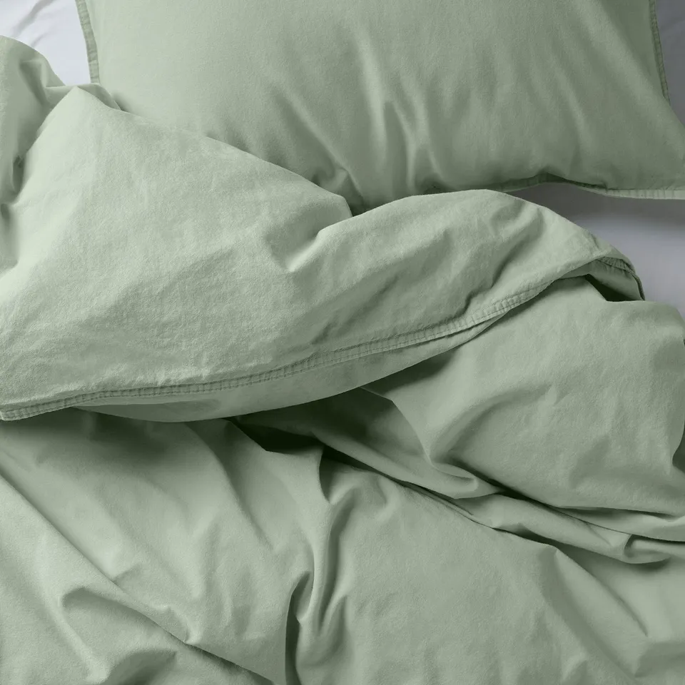 Soft green bedding set, made of smooth, recycled cotton, neatly arranged, showcasing softness and comfort.