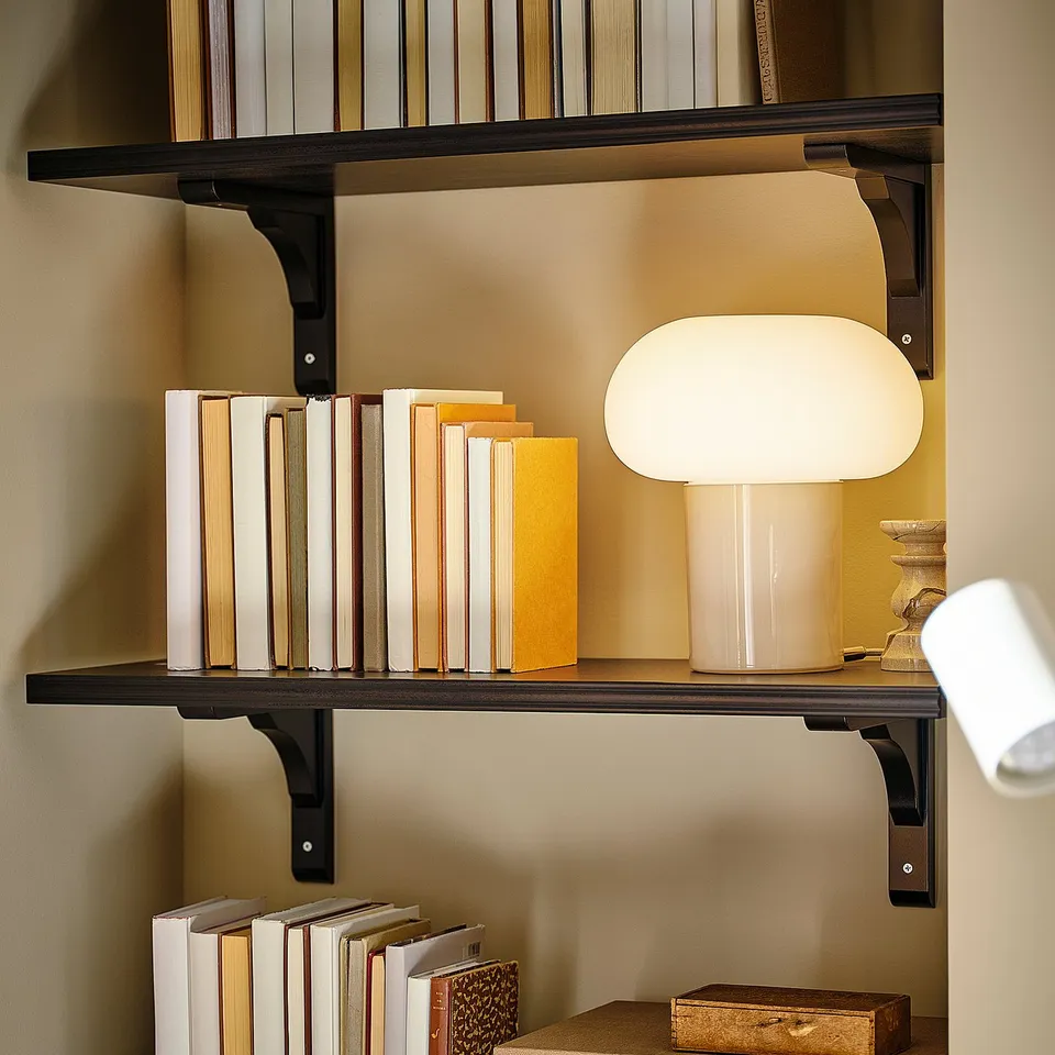 Bookshelf with black metal supports holds books and lamp.