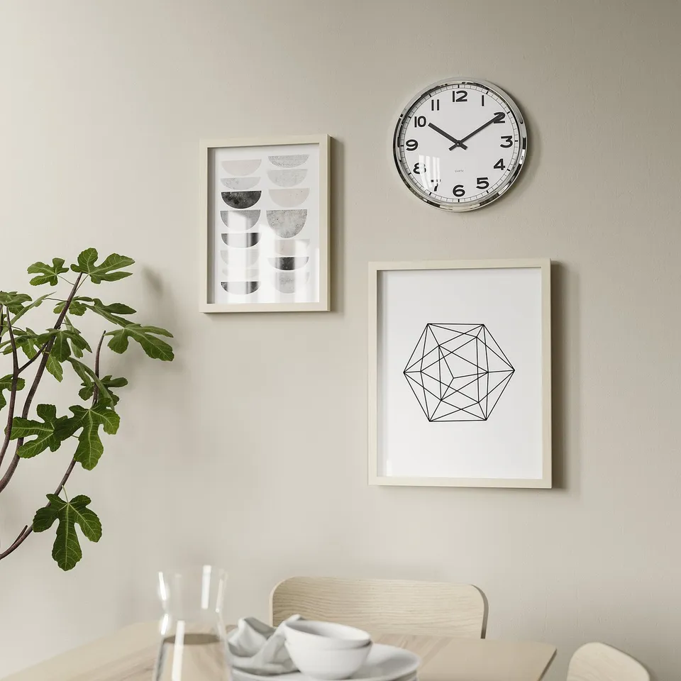 Minimalist clock, art, plant above wooden table with white setting.
